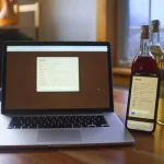 A picture of the software "bevdb" running on a laptop and iPhone, sitting on a table with three bottles of mead