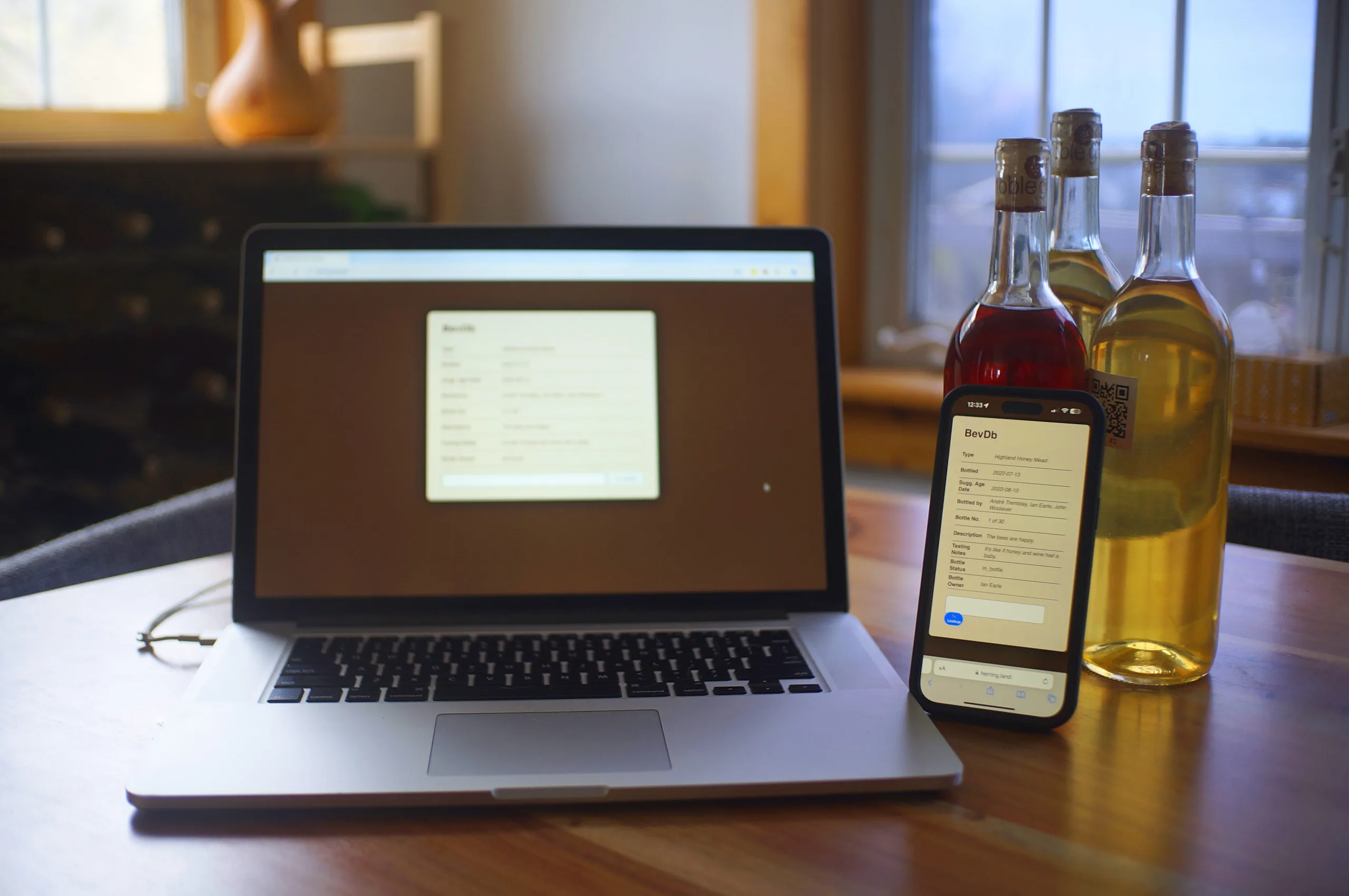 A picture of the software "bevdb" running on a laptop and iPhone, sitting on a table with three bottles of mead